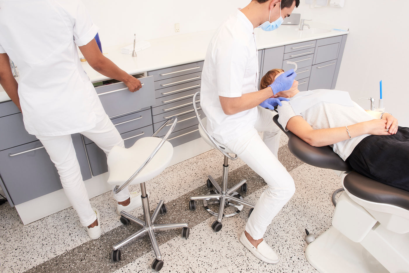 Tandklinik med tandlæge der sidder på InCharge stol med fodbetjening. Klinikassistent står ved siden af sin InCharge operatørstol. Patient ligger i patientstol.