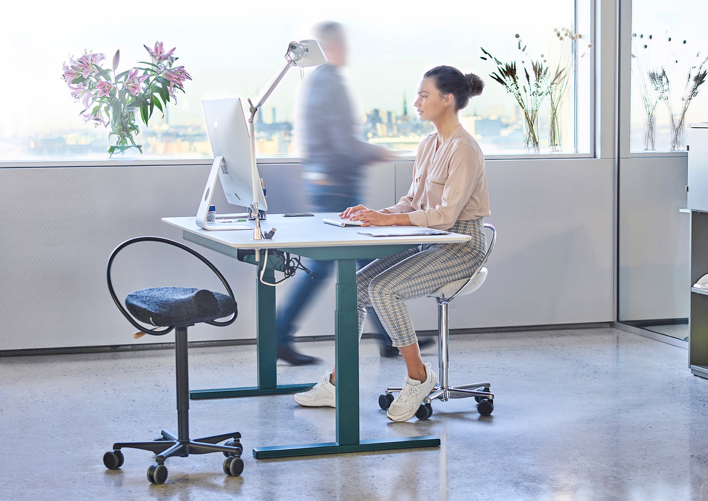 Kvinde sidder på en InCharge Office betrukket med lysegrå Hallingdal uld fra Kvadrat. Hun sidder på et kontor og arbejder ved sin IMac.